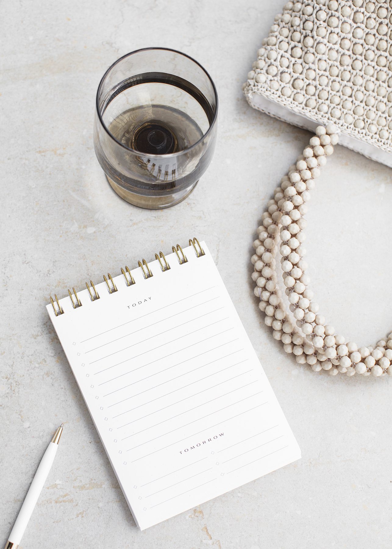 Pearl purse beside a white notebook and glass of red wine